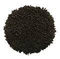 A pile of small dark brown to black seeds or granules photographed from above on a plain white background.