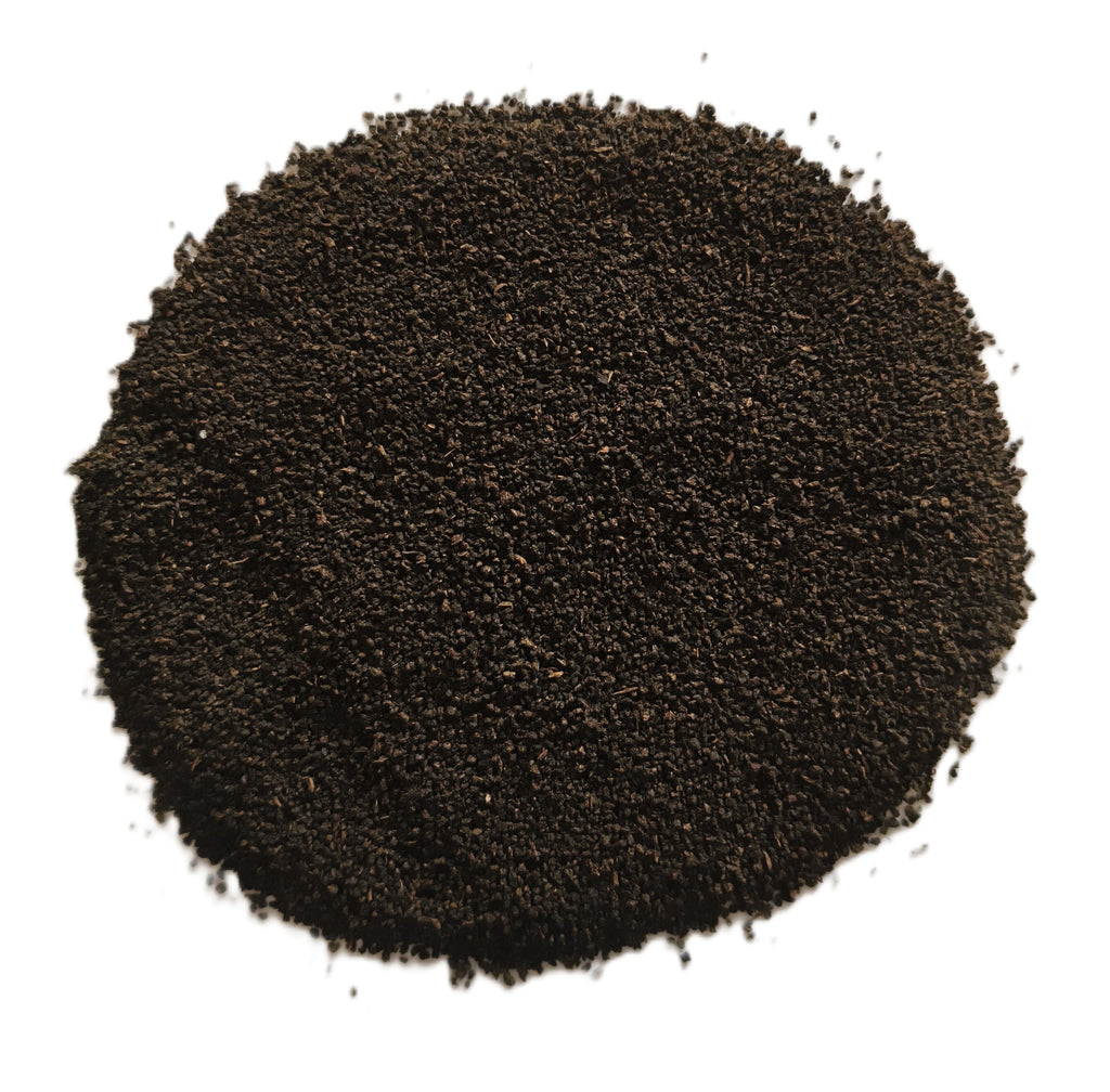 A circular pile of dark brown to black granular powder or seed-like material on a plain white background.
