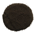 A circular pile of dark brown to black granular powder or seed-like material on a plain white background.