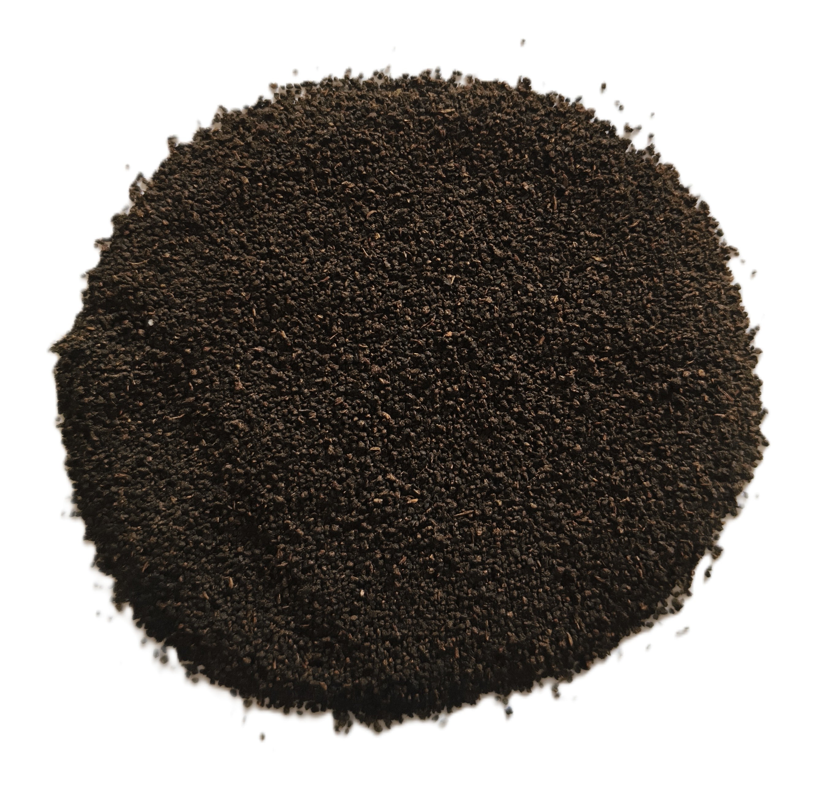 A circular pile of dark brown to black granular powder or seed-like material on a plain white background.