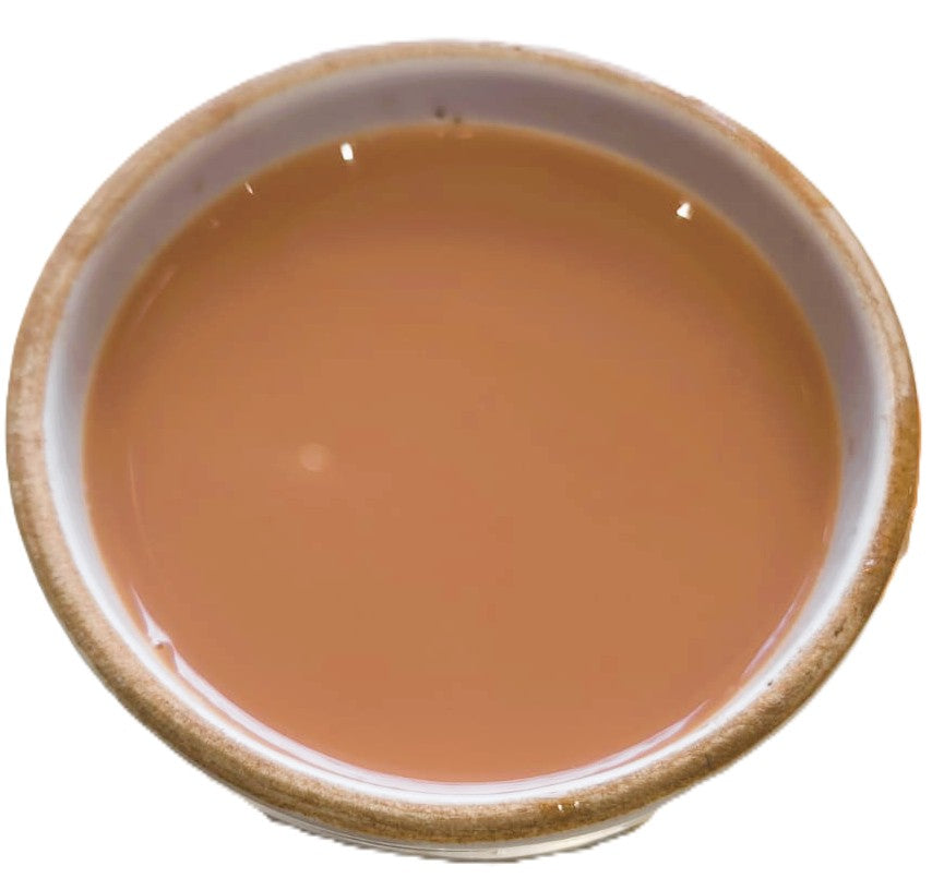 A top-down view of a light brown liquid, likely tea or coffee, served in a small rustic ceramic bowl against a white background.
