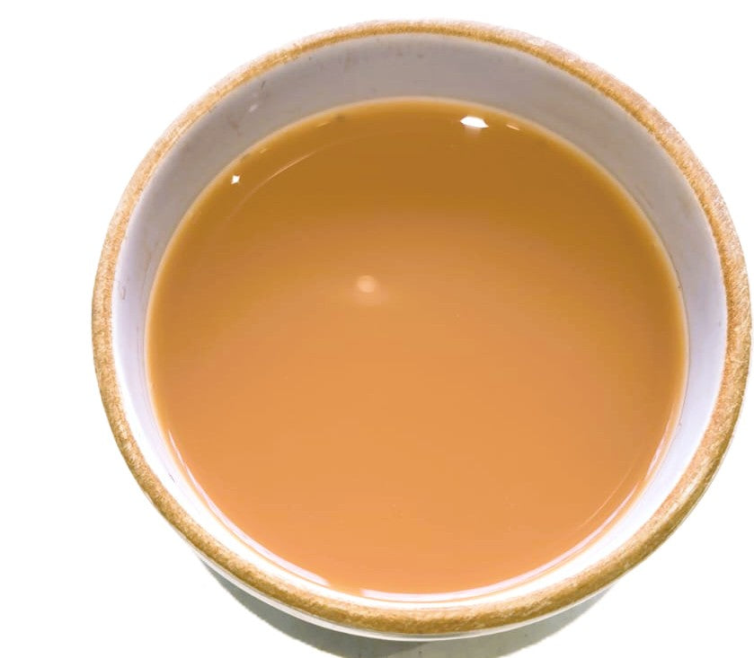A top-down view of a light brown liquid, likely milk or tea, in a white ceramic bowl with a textured beige rim, set against a plain white background.