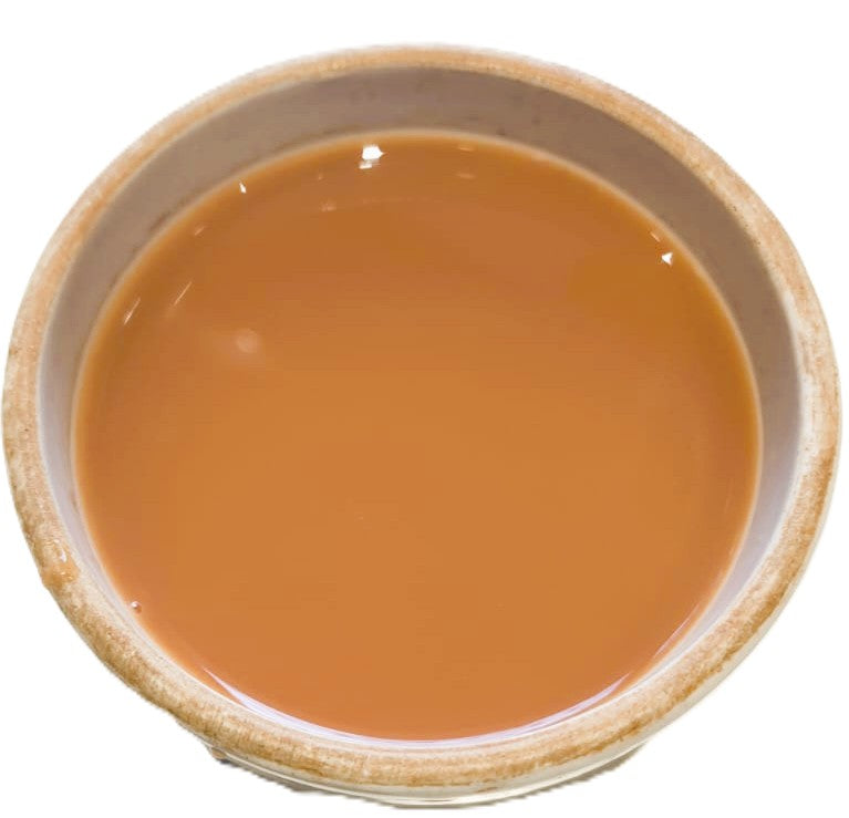 A top-down view of a light brown liquid, likely tea or coffee, served in a rustic beige ceramic bowl against a plain white background.